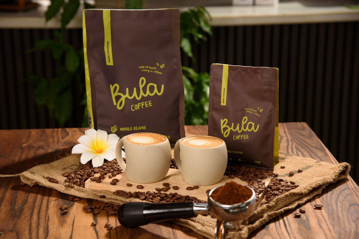 Bula Coffee 1kg and 200g whole bean bags with two lattes and a frangipani
